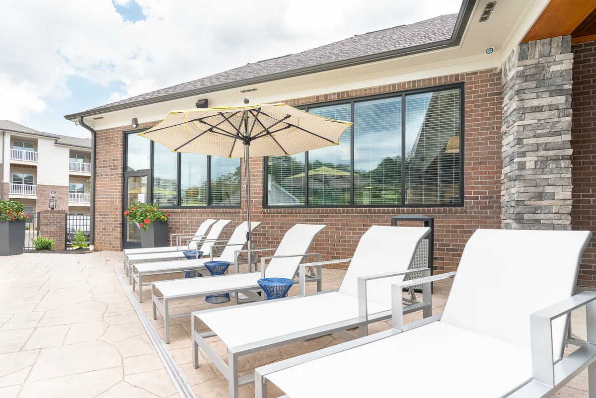 This image features an outdoor lounge area equipped with comfortable chairs, umbrellas, vibrant flower pots, and a view of the building's windows. The space is tranquil and conducive to relaxing, reading, or socializing outdoors.