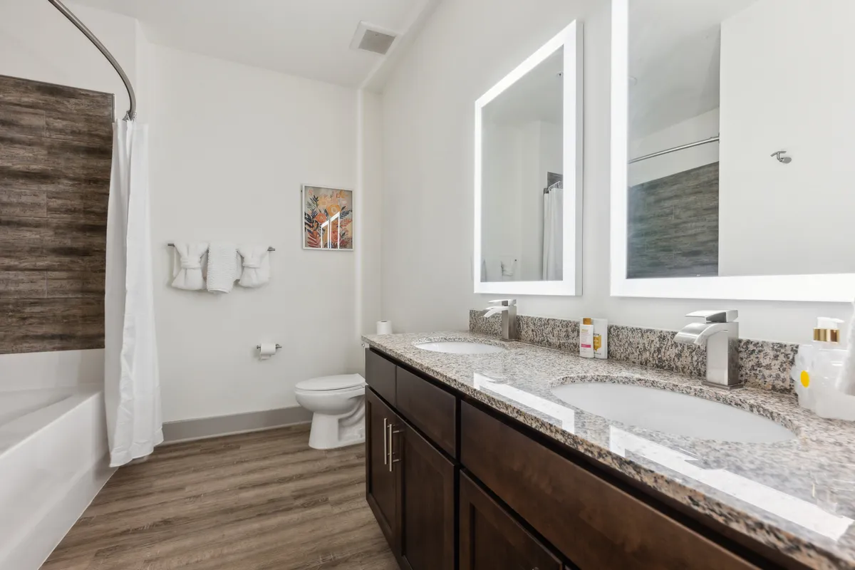 A bright, modern bathroom featuring a double sink vanity with framed mirrors above, a spacious bathtub, tasteful wall art, and plenty of sunlight. The clean lines and quality fixtures convey a refreshing and upscale ambiance.