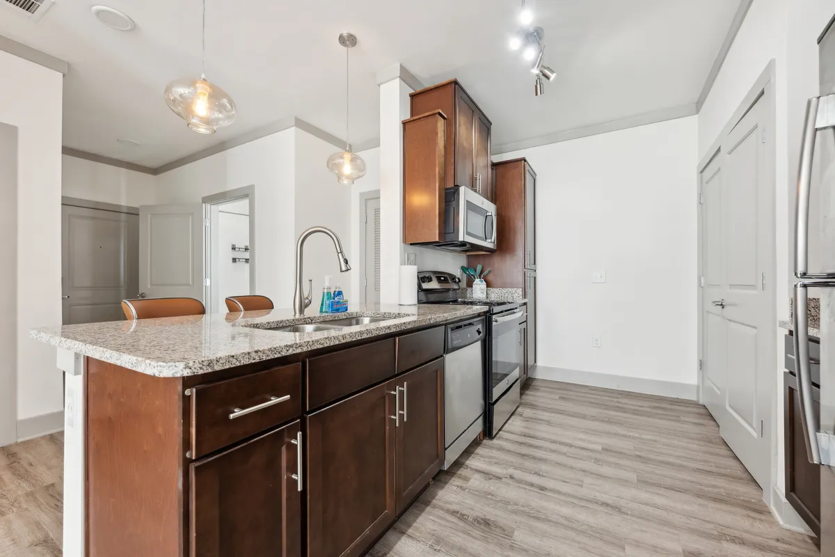 A bright, modern kitchen with granite countertops, stainless steel appliances, and chic light fixtures. The space exudes a sense of readiness for both everyday meals and special occasions, highlighting the functionality and elegance of the kitchen setting.