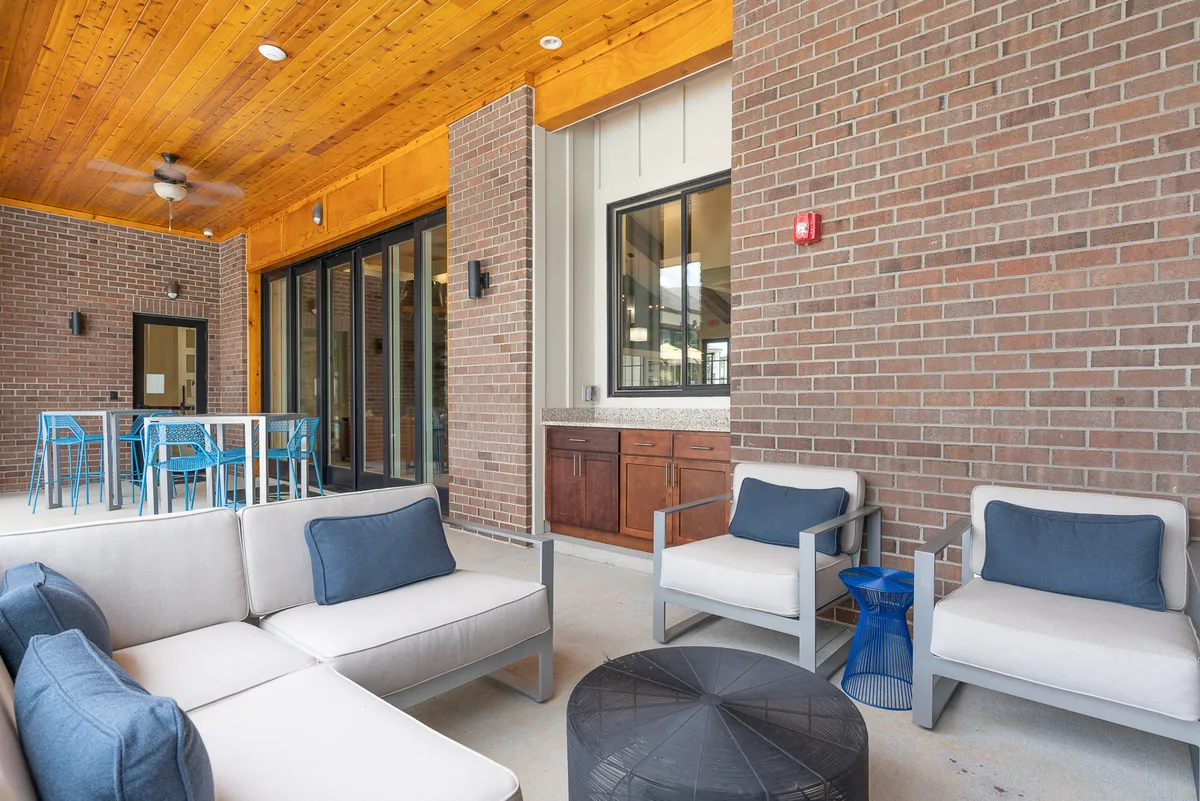 An open-plan dining and living area with a comfortable sofa, blue bar stools at a counter, and a modern ceiling. The dining space seamlessly connects with the kitchen, creating a social atmosphere ideal for shared meals and lively conversations.