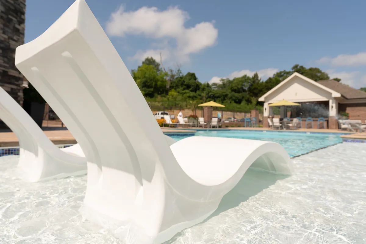 An inviting pool area with lounge chairs, sun umbrellas, and the clubhouse in the background, bathed in soft natural light. The space feels serene and social, illustrating opportunities for relaxation and informal networking after work hours.