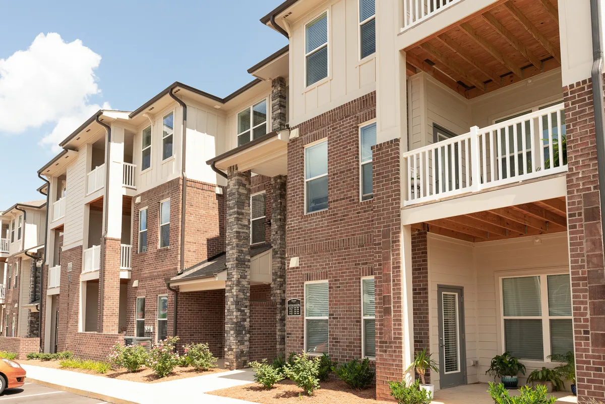 A wider exterior view featuring brick façades, stone accents, balconies, and a landscaped garden. The image conveys both connectivity and relaxation, with outdoor spaces suggesting a harmonious balance between a productive business environment and serene living.