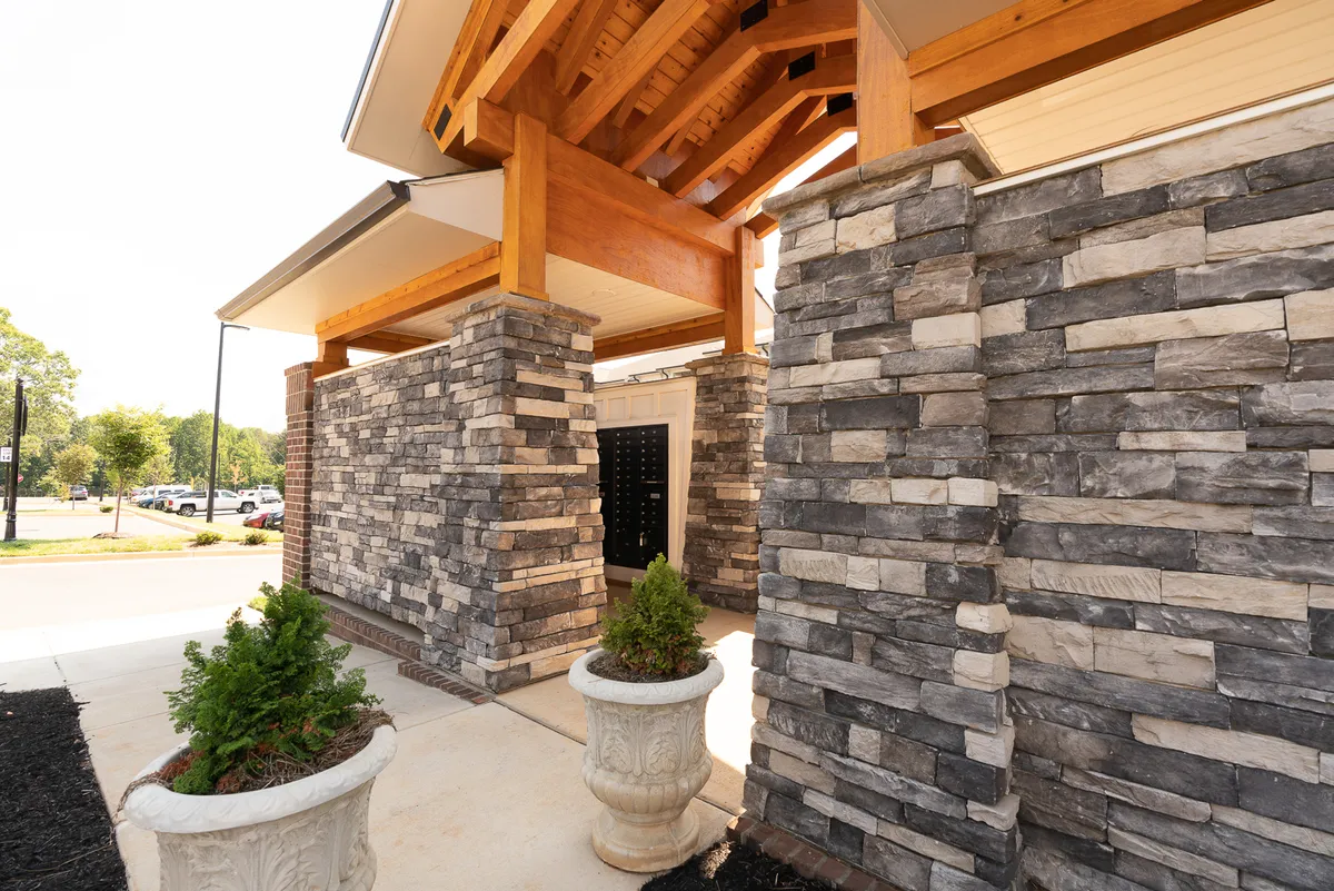 The image captures the inviting exterior entrance of Overlook 3005, featuring stone walls, robust wooden beams, and thoughtfully arranged planters. The setting is warm and welcoming, suggesting a sense of arrival and community.
