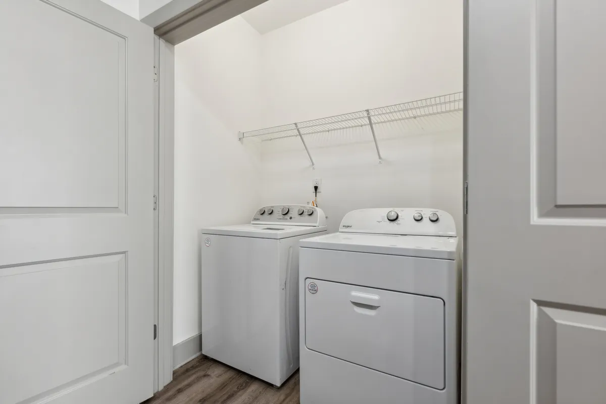 A practical laundry area, featuring a modern washer and dryer with shelving above for organization. The space is tidy, efficient, and clearly designed to simplify home management tasks.